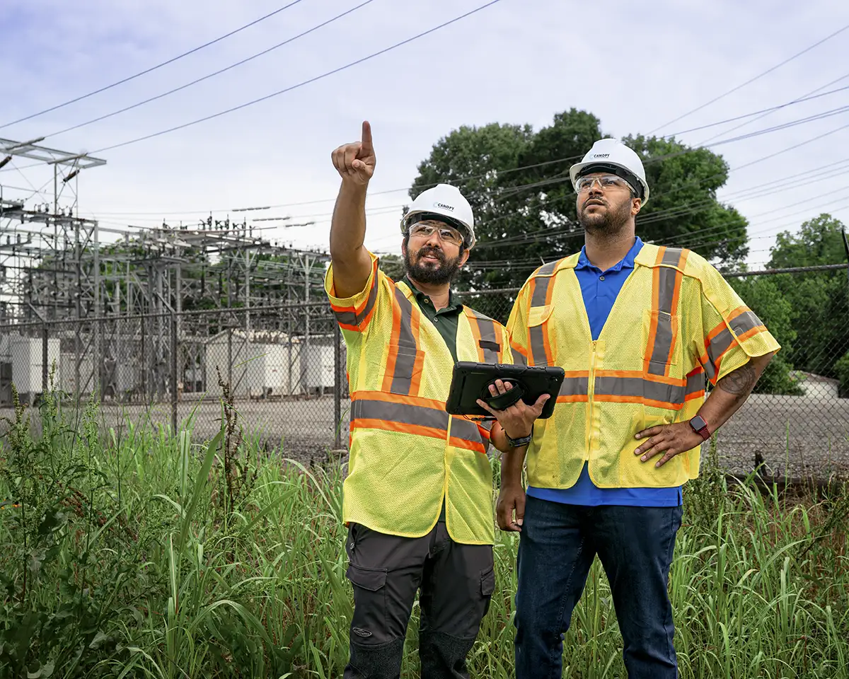 Utility workers in safety gear evaluating an electrical substation infrastructure.